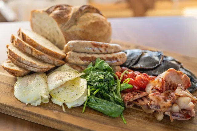 Cooked breakfast board with eggs, bacon, sausages, spinach, mushrooms and sourdough