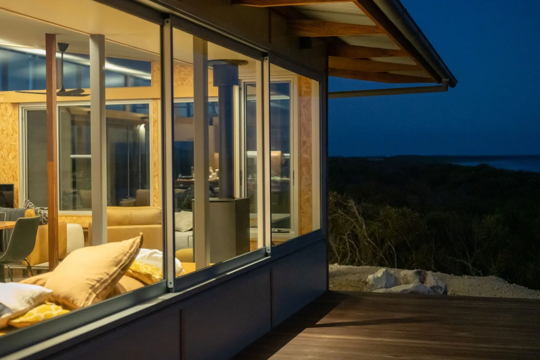 The house glowing behind glass at dusk above the coastal heath